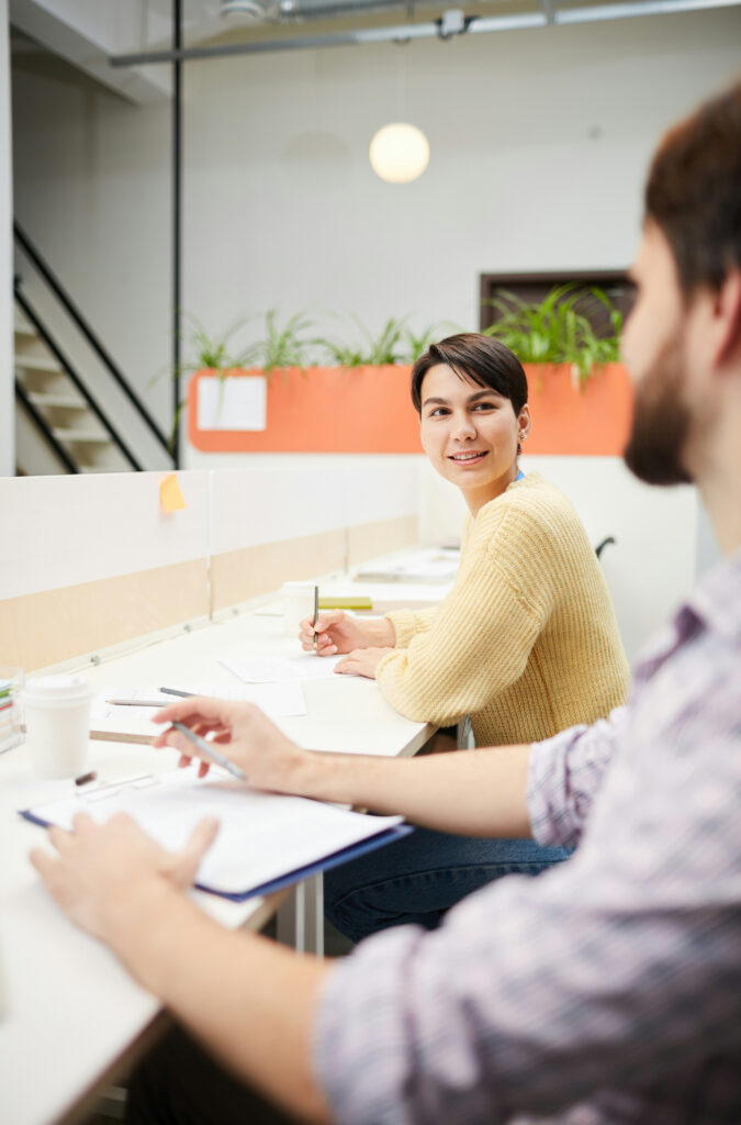 Woman looking back a male team member while working with a pencil and paper at a desk in an office